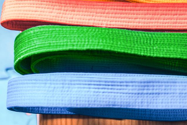 Bunte, aufgerollte Gürtel in verschiedenen Farben liegen übereinander auf einem Holztisch.