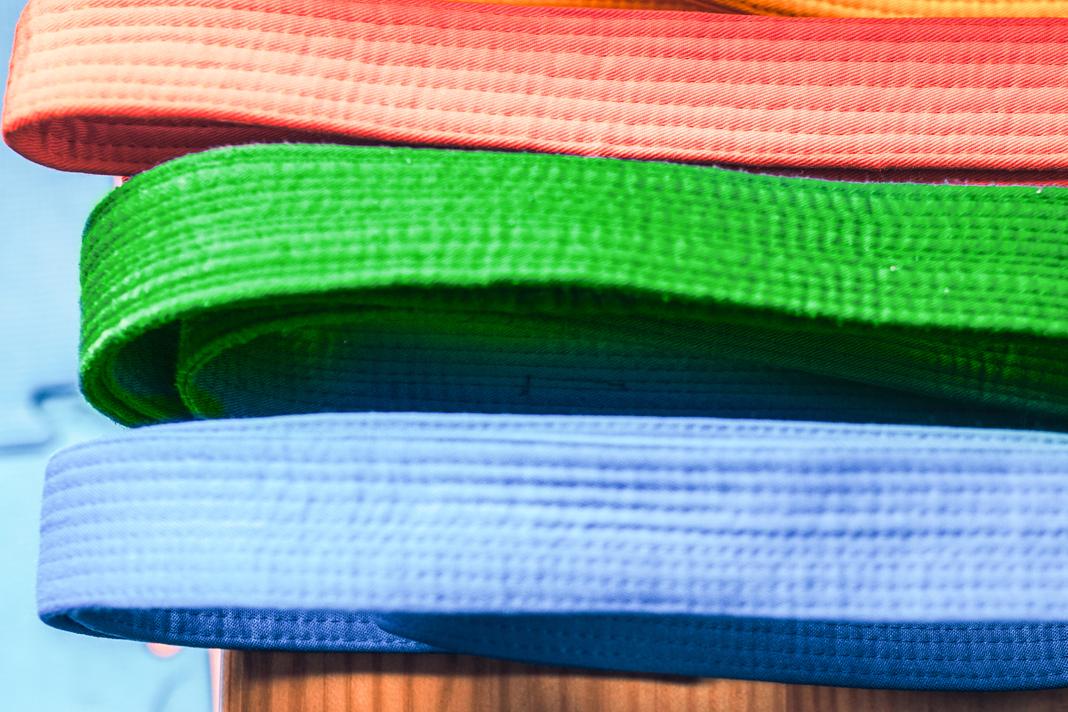 Bunte, aufgerollte Gürtel in verschiedenen Farben liegen übereinander auf einem Holztisch.