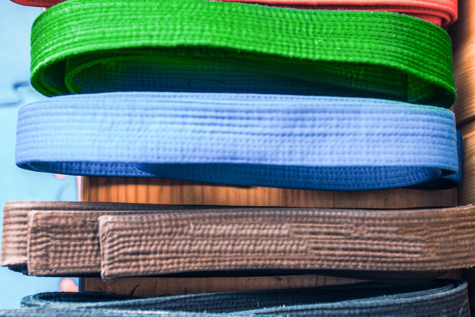 Bunte, aufgerollte Gürtel in verschiedenen Farben liegen übereinander auf einem Holztisch.