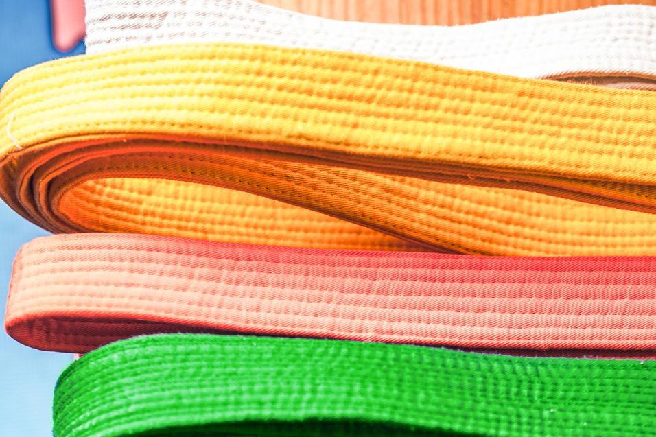 Bunte, aufgerollte Gürtel in verschiedenen Farben liegen übereinander auf einem Holztisch.