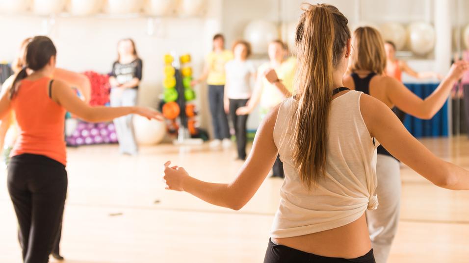 Gruppe von Frauen in Sportkleidung beim Tanztraining in einem gut beleuchteten Fitnessraum mit Spiegeln.